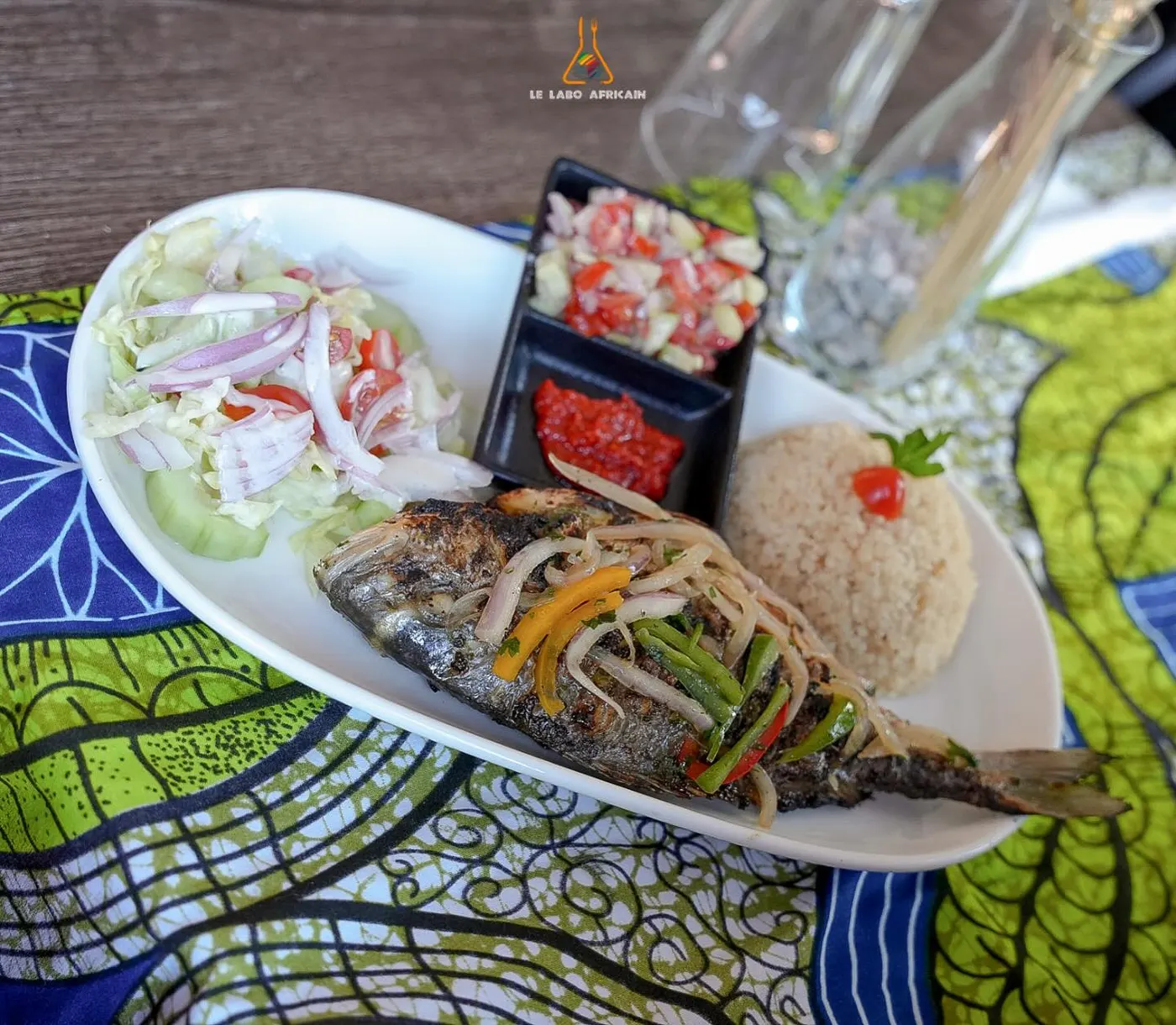 A whole fish plate with vegetables on a wax-print tablecloth