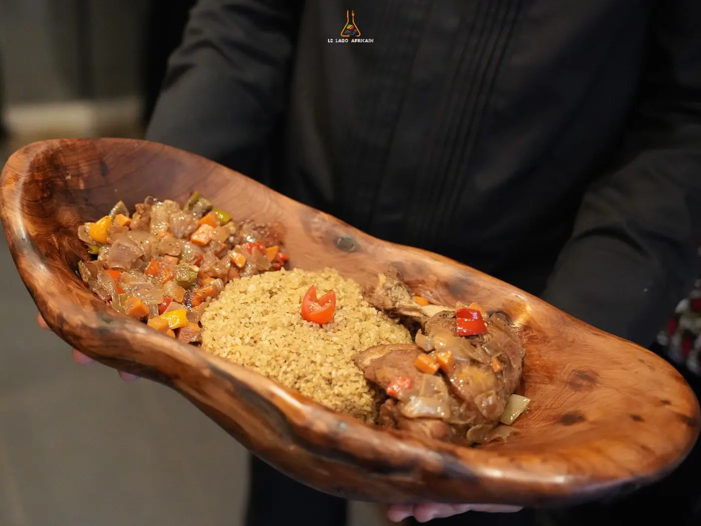 A carved wooden bowl of seasoned rice with fried chicken