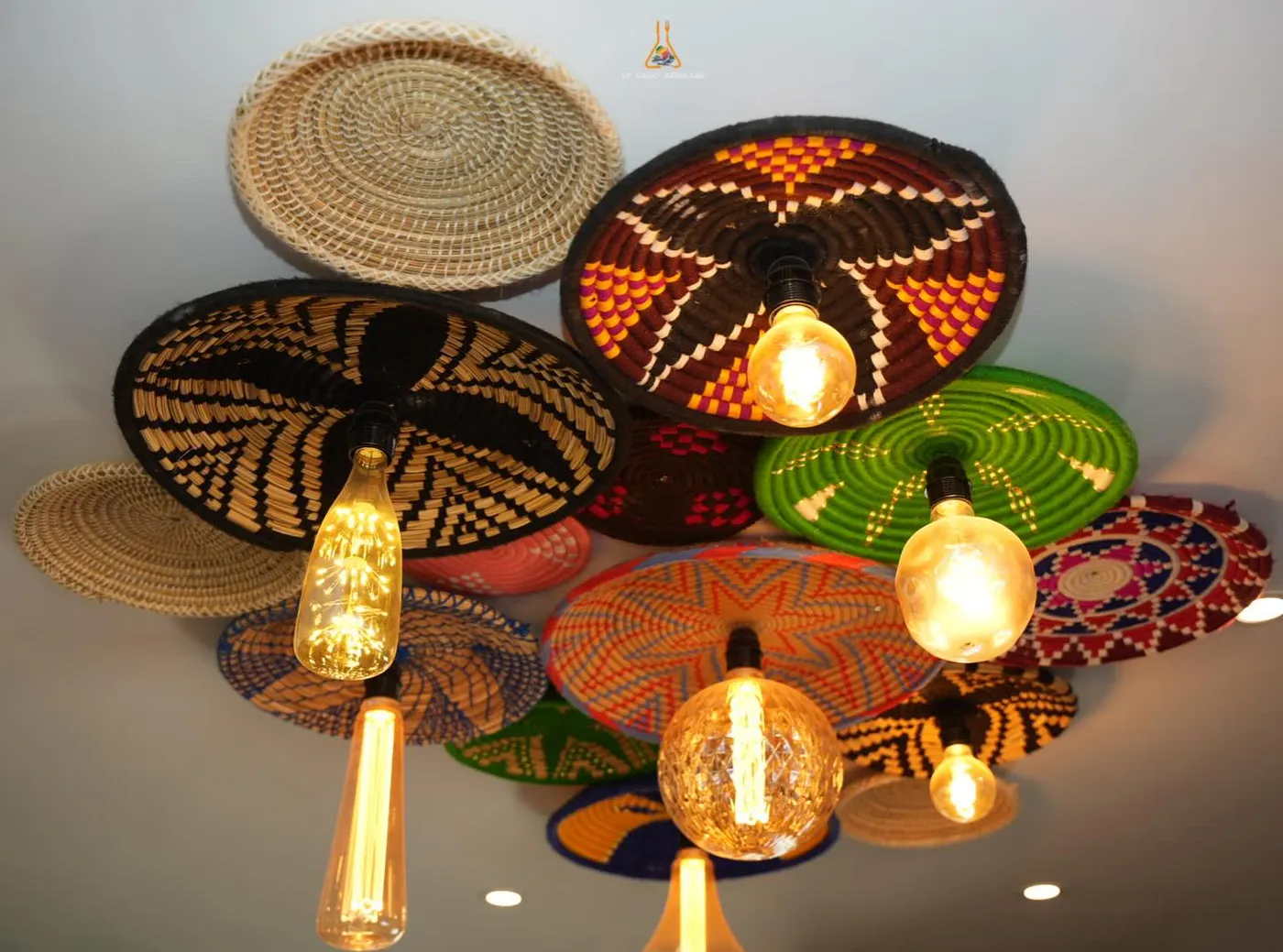 A ceiling of colourful woven basket lamps with glowing filament bulbs